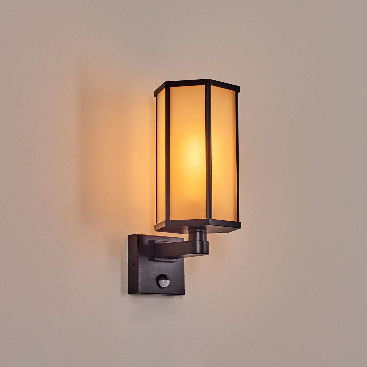 Eine schwarze, rechteckige Wandleuchte mit einem Schirm aus Milchglas. Die Lampe ist an einer beigen Wand montiert. Das Licht ist an.
