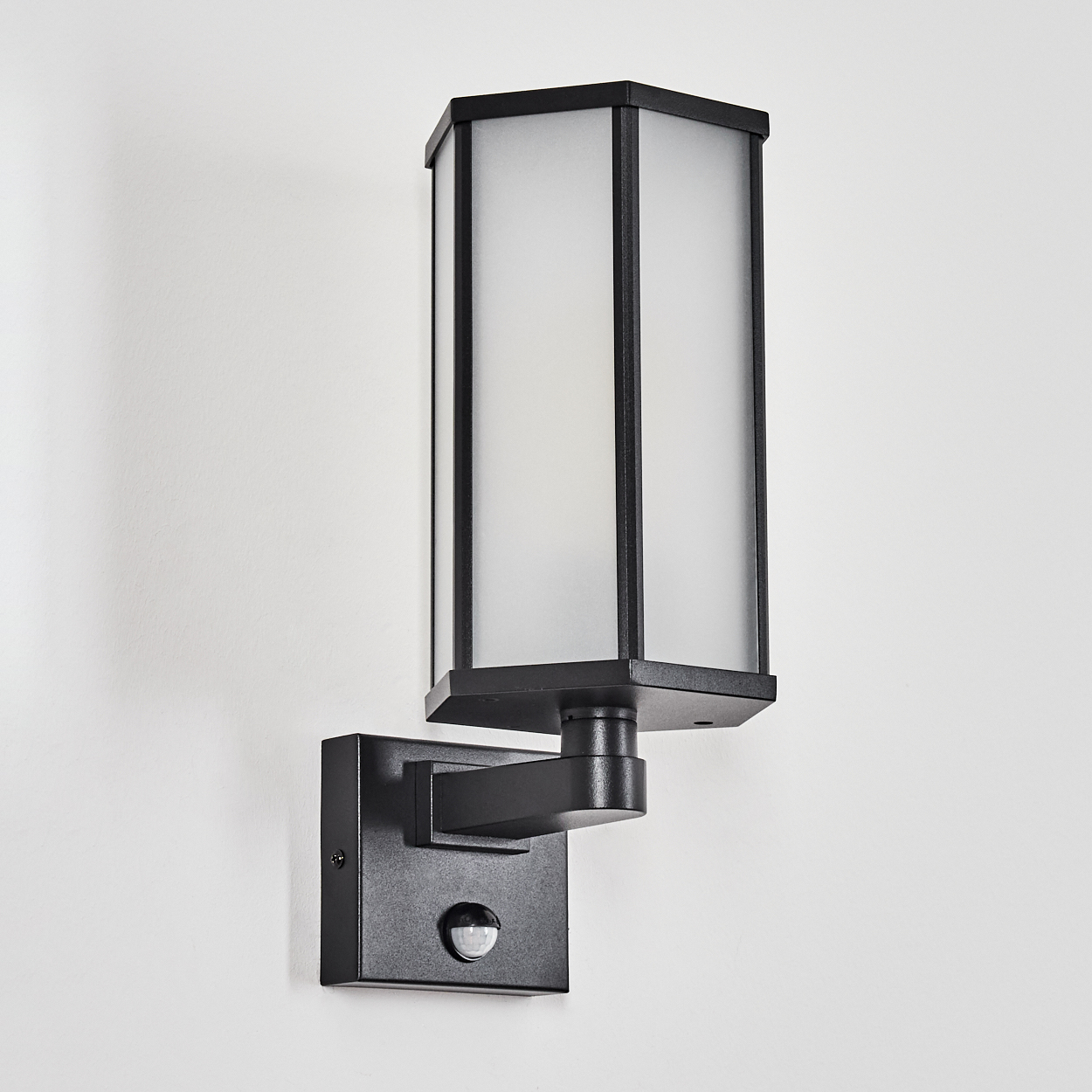 Schwarze Außenwandleuchte an weißer Wand. Rechteckige Lampe mit Milchglas und Bewegungssensor.