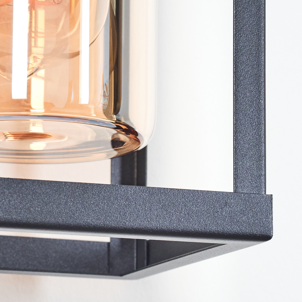 Nahaufnahme einer modernen Leuchte. Sie hat ein Glasgehäuse mit einer warm getönten Glühbirne in einem schwarzen Metallrahmen.