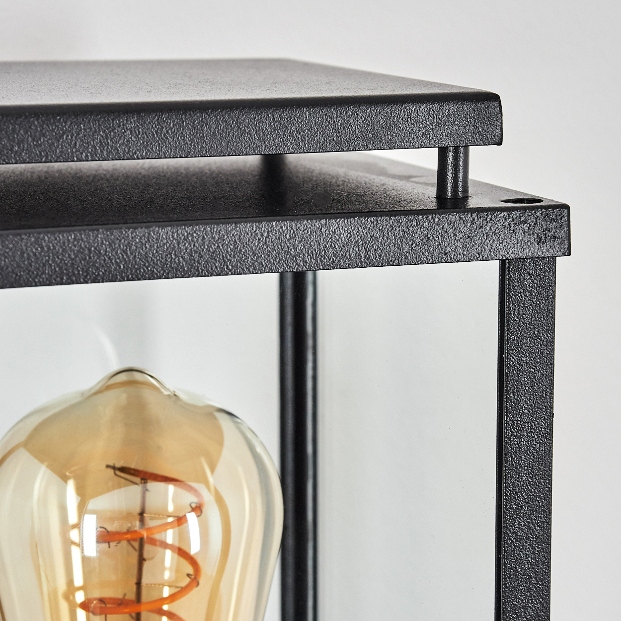 Nahaufnahme einer schwarzen Metalllaterne mit Glaseinfassung. Im Inneren befindet sich eine Glühbirne. Der Hintergrund ist weiß.