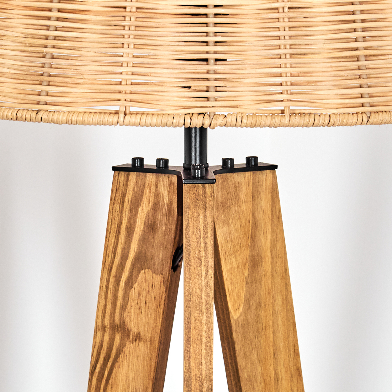 Nahaufnahme einer Lampe. Sie hat einen gewebten Lampenschirm und Holzbeine. Die Beine sind dreieckig und braun gebeizt.