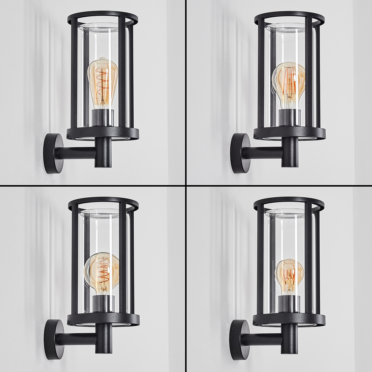 Vier wandmontierte schwarze Lampen mit klarem Glas und leuchtenden Glühbirnen vor einer weißen Wand. Die Lampen sind identisch.