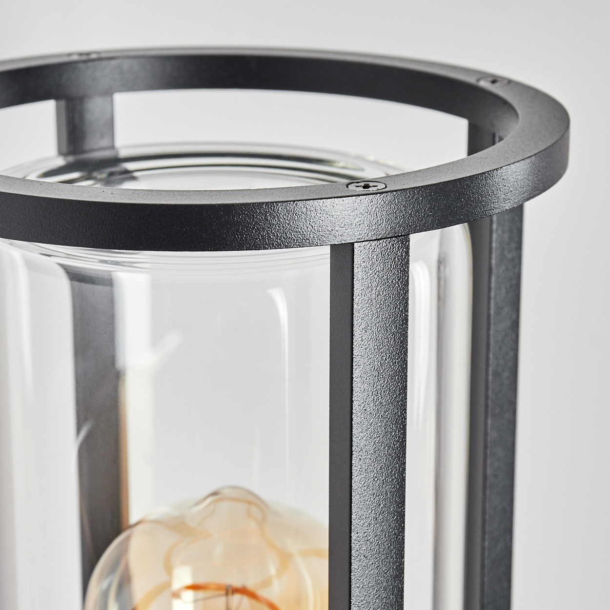 Nahaufnahme einer schwarzen Metalllaterne. Ein Glaszylinder umschließt eine Glühbirne. Der obere Ring ist schwarz.