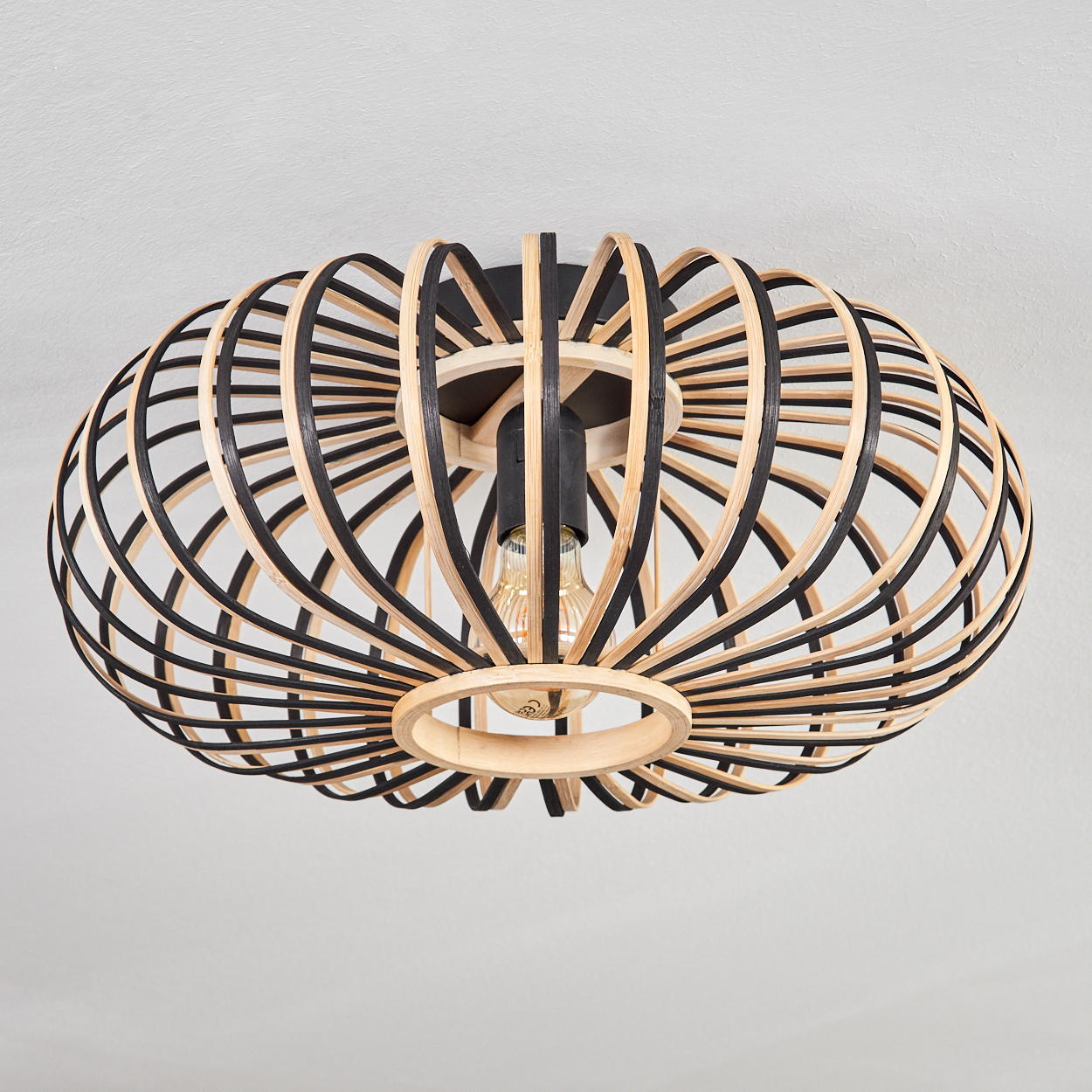 Eine hölzerne, käfigartige Deckenlampe mit schwarzen und hellbraunen Bögen. Die Lampe enthält eine sichtbare Glühbirne vor einer weißen Decke.