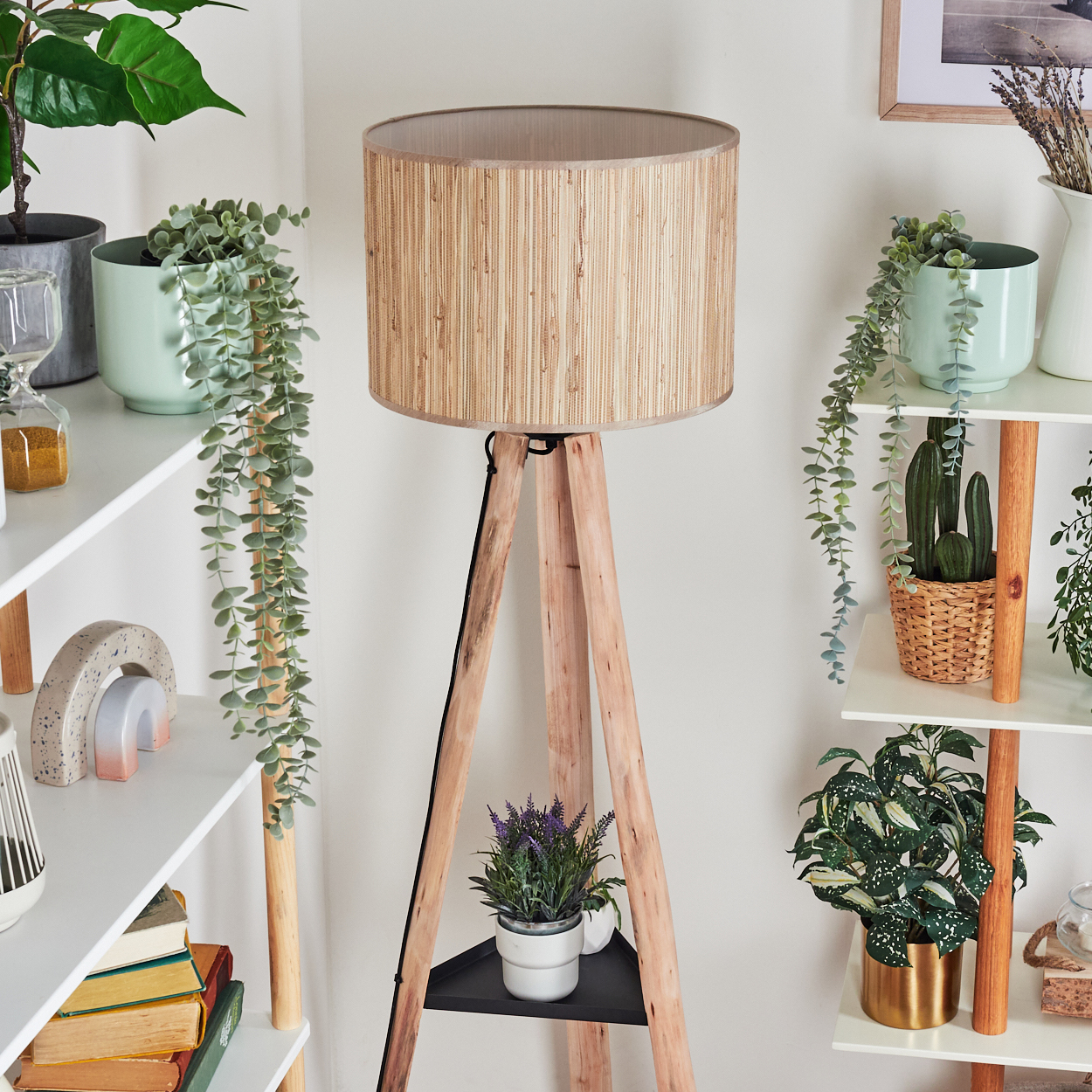 Eine Holzstativlampe steht in der Nähe von Regalen mit Pflanzen und Dekoration. Unter der Lampe befindet sich eine Lavendelpflanze.