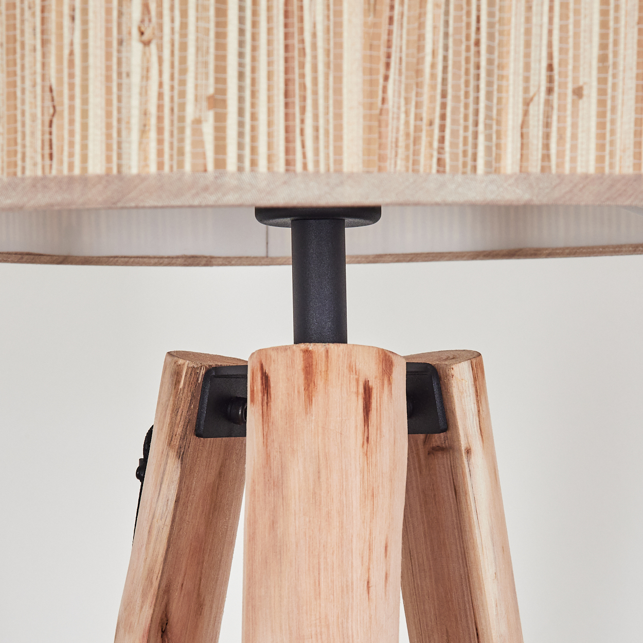 Nahaufnahme einer Holzstativlampe. Der Lampenschirm besteht aus gewebtem Material. Der Sockel ist hellbraunes Holz.