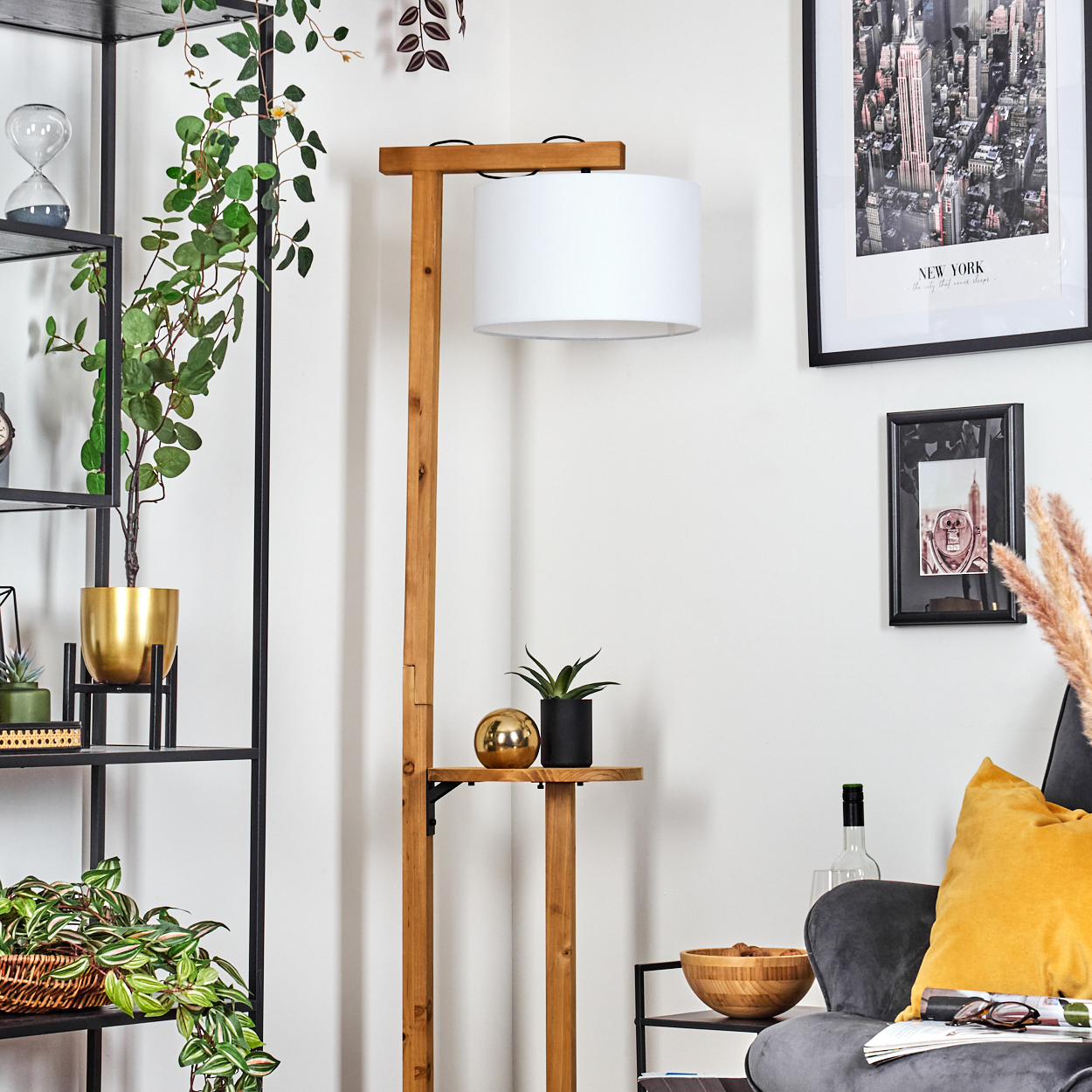 Wohnzimmer mit Holz-Stehlampe, Pflanzen, schwarzem Regal und grauem Sessel mit gelbem Kissen.