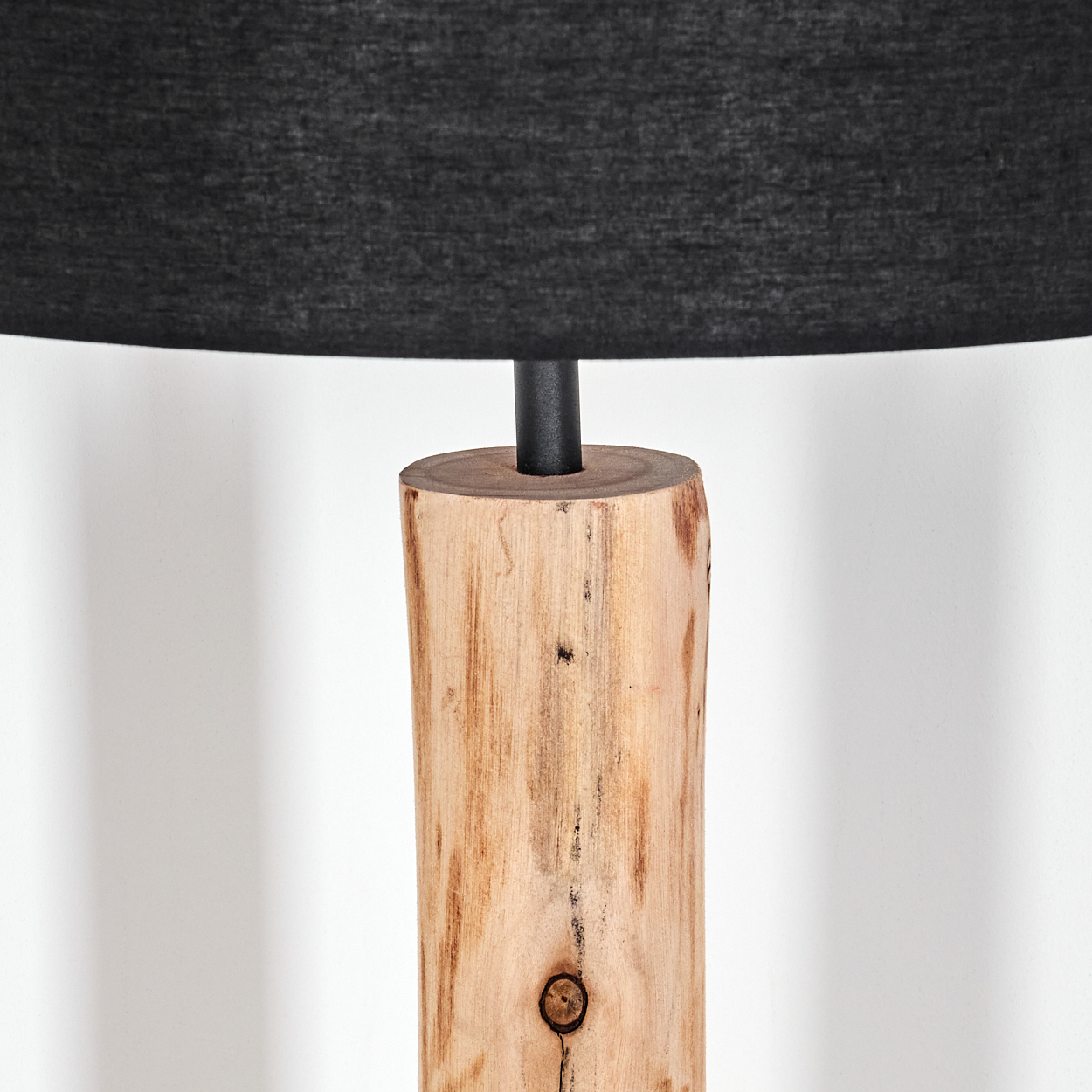 Ein Holzlampensockel trägt einen schwarzen Lampenschirm. Der Sockel ist zylindrisch, mit sichtbarer Holzmaserung und einem Knoten. Der Hintergrund ist weiß.
