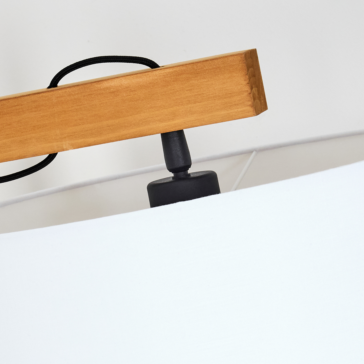 Eine Holzlampenhalterung mit schwarzem Kabel und Schirm. Der Schirm ist weiß. Die Halterung befindet sich vor einer weißen Wand.