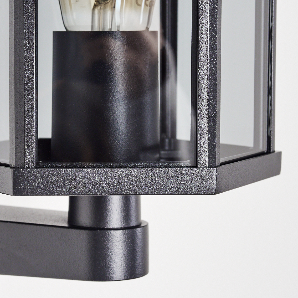 Nahaufnahme einer schwarzen Außenlampe. Glasscheiben umschließen eine Glühbirne. Die Lampe hat einen quadratischen Rahmen und einen gebogenen Arm.