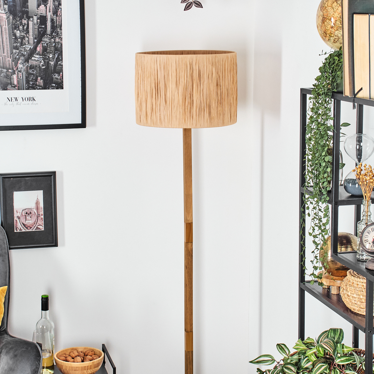 Ein Raum mit einer hohen Lampe, Bildern und einem Regal mit Pflanzen und Dekorationsartikeln.