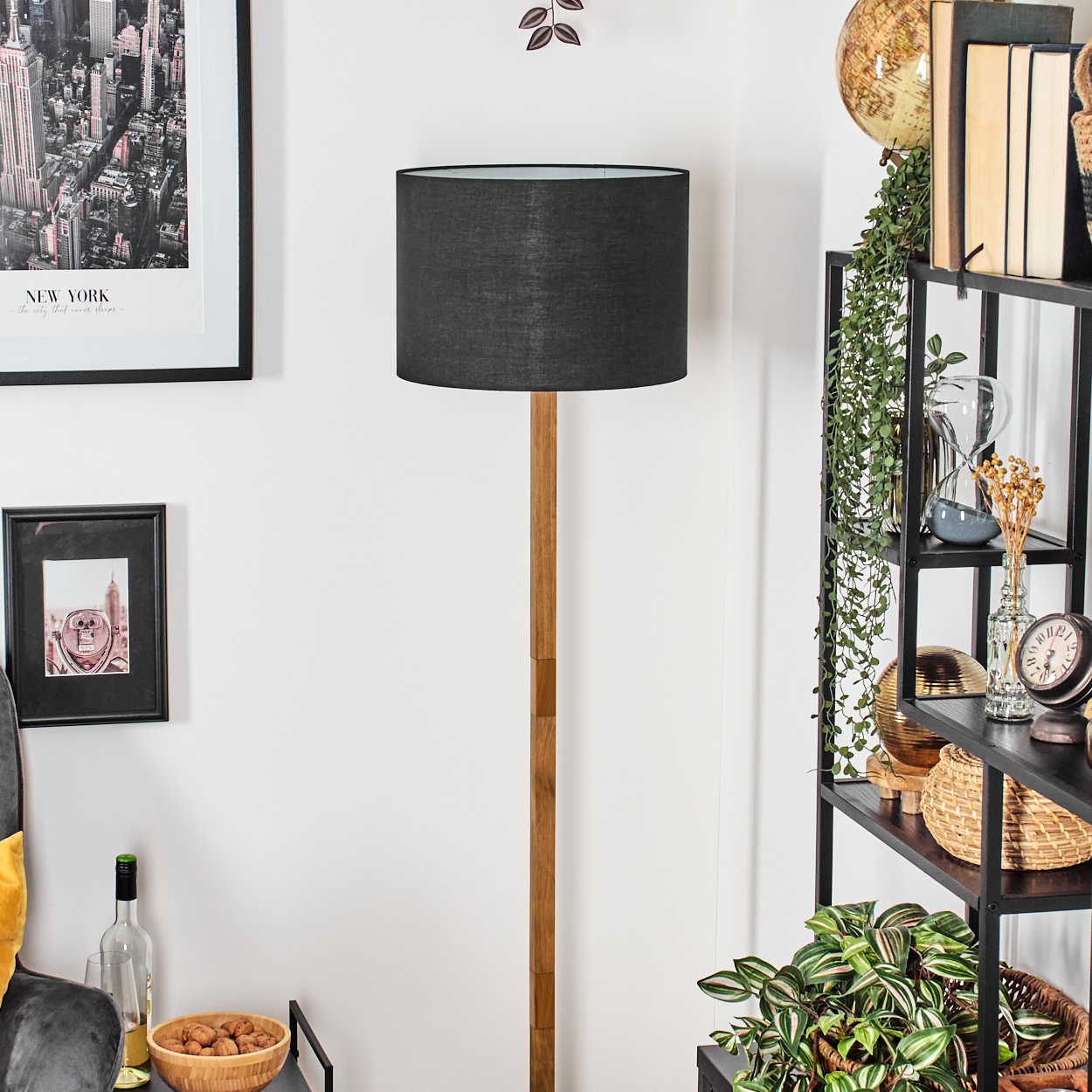 Ein Raum mit einer schwarzen Lampe, einem Regal mit Dekorationen und Bildern von New York. Die Lampe ist aus Holz.