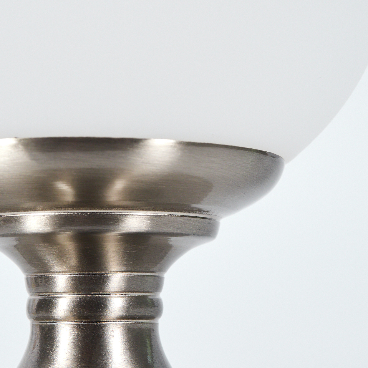 Nahaufnahme eines Lampensockels. Die Lampe hat einen silbernen Metallsockel, der einen runden, mattierten Glasschirm vor weißem Hintergrund trägt.