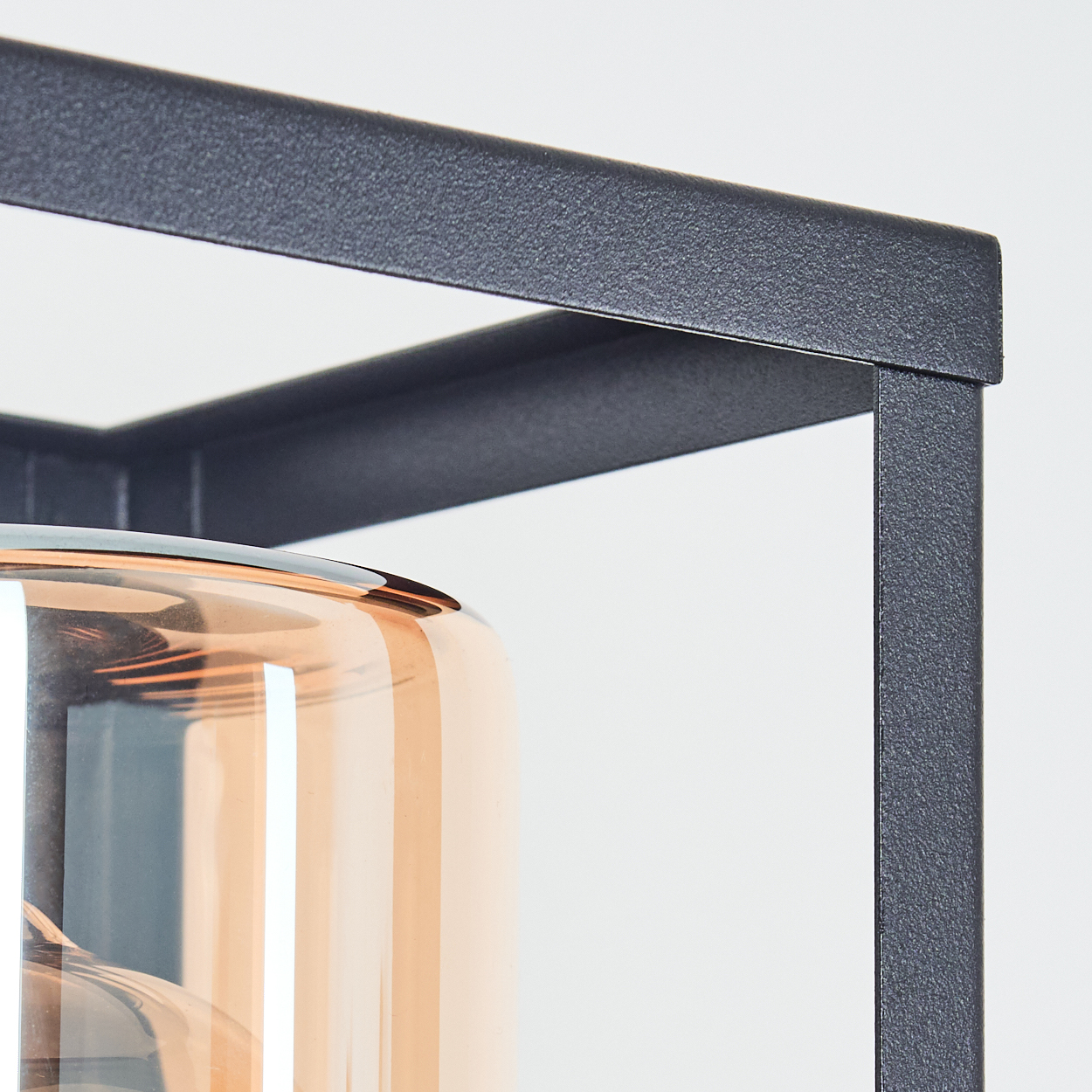 Nahaufnahme einer Lampe mit dunklem Metallrahmen. Ein runder, bernsteinfarbener Glasschirm reflektiert Licht. Weißer Hintergrund.