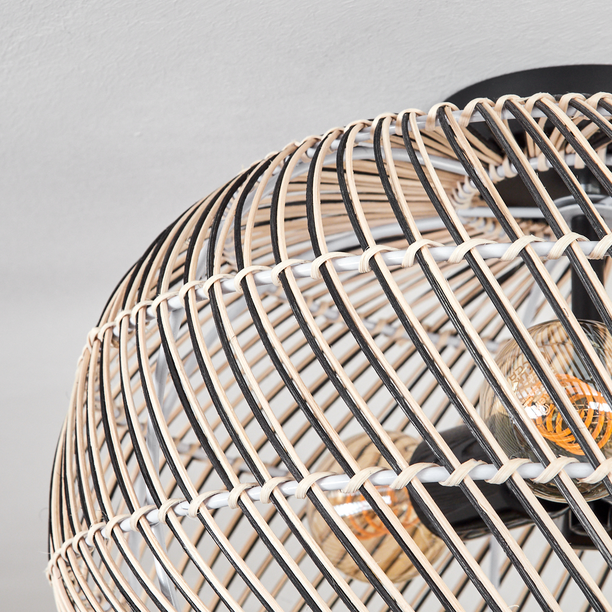 Nahaufnahme eines gewebten Lampenschirms aus Rattan mit schwarzen und beigen Streifen und freiliegenden Glühbirnen.