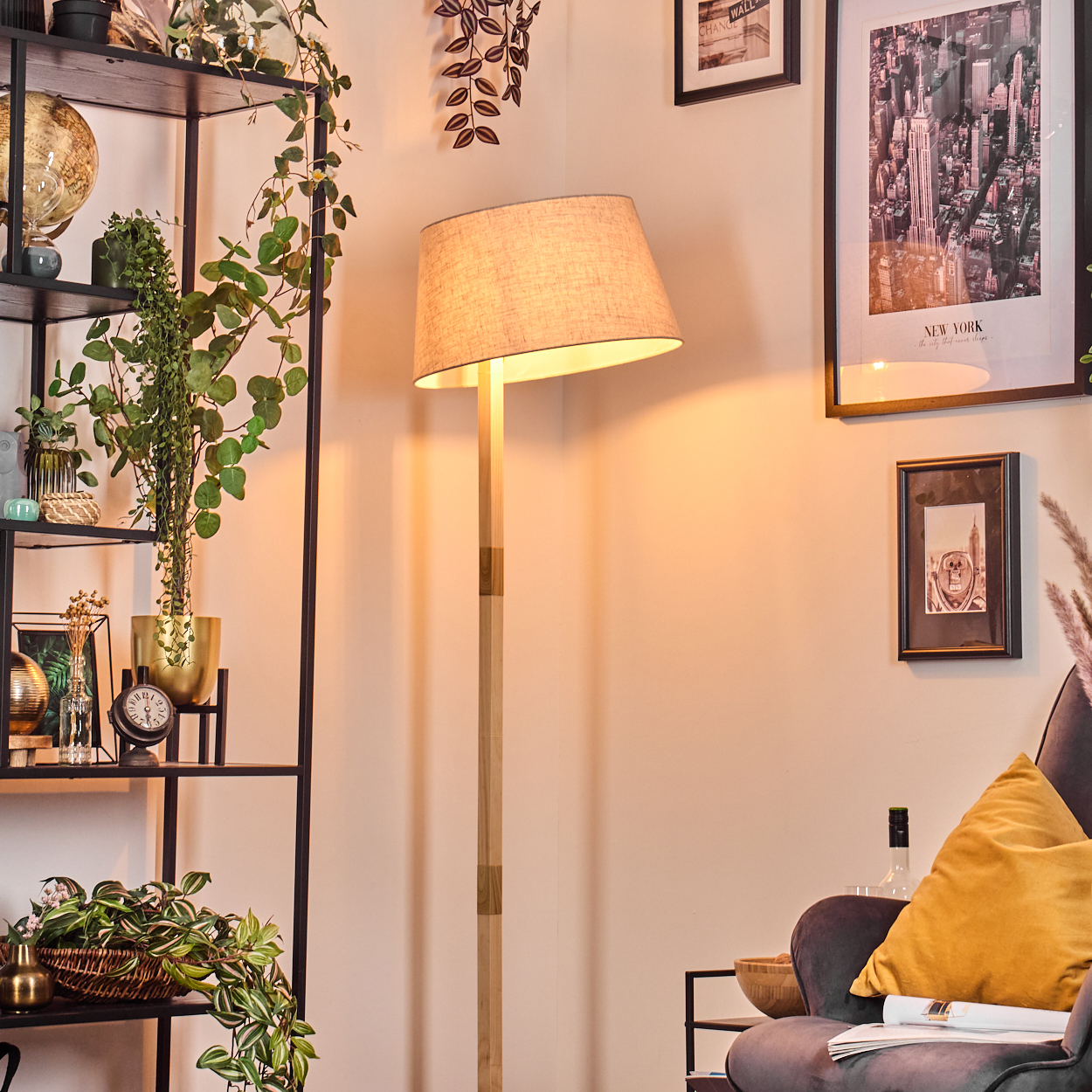 Wohnzimmerecke mit Stehlampe, schwarzen Regalen mit Pflanzen und Dekoration, grauem Sessel und New York-Bild.