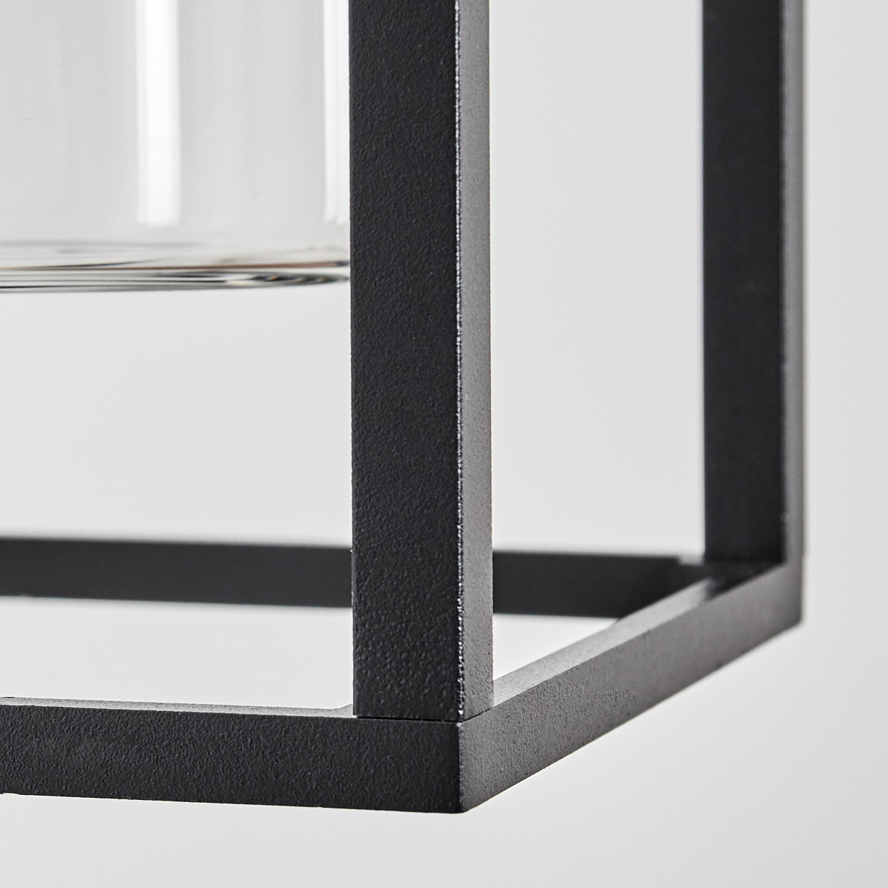Nahaufnahme eines schwarzen Metallwürfelrahmens mit einem Glasobjekt im Inneren, vor weißem Hintergrund.