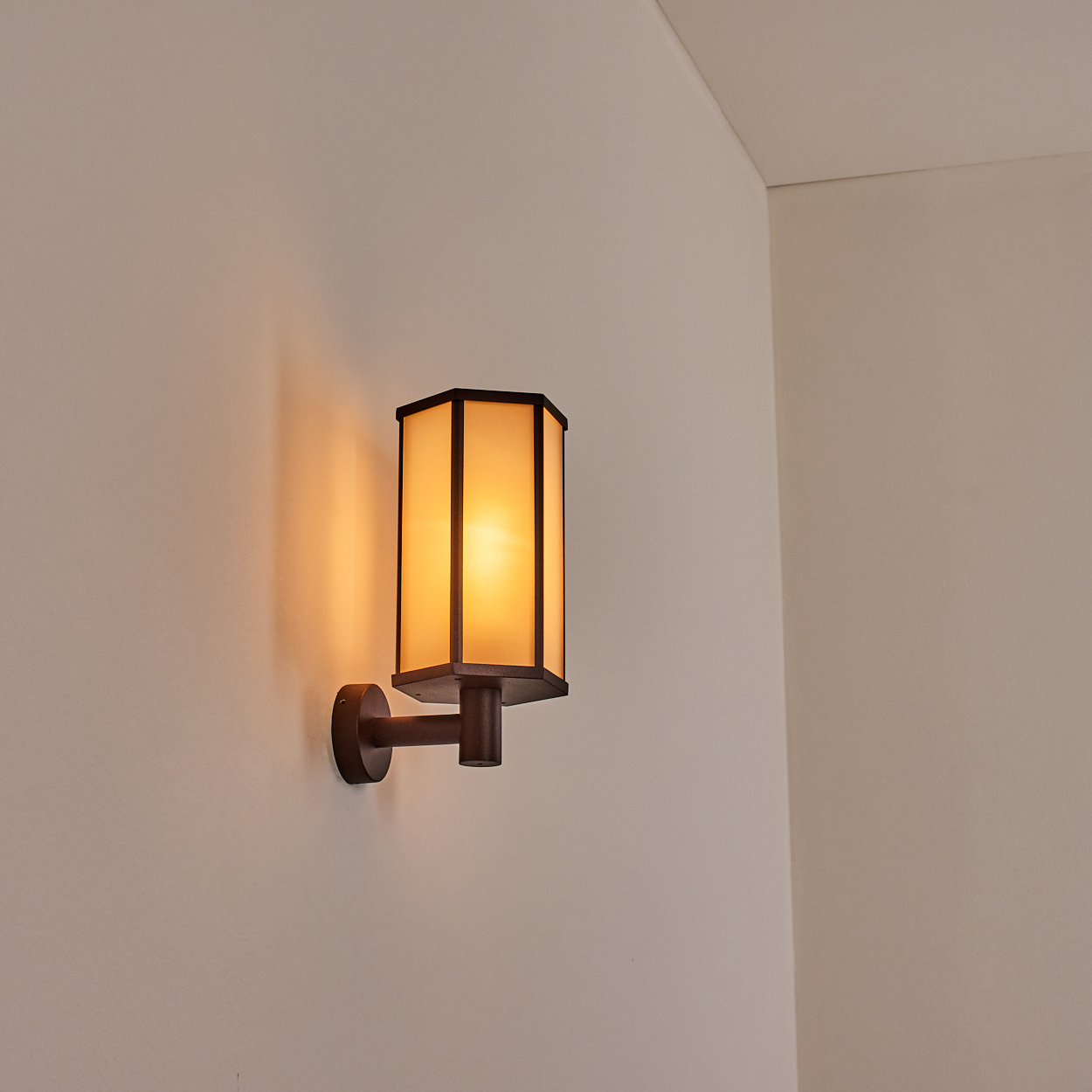 Eine an der Wand montierte, rechteckige Lampe mit braunem Rahmen und gelbem Licht, vor einer weißen Wand.