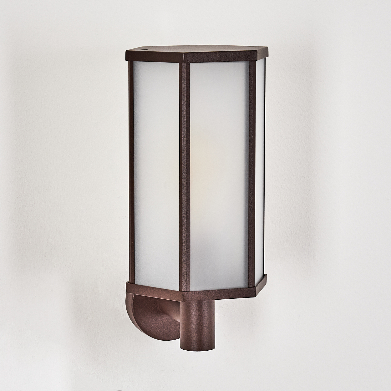 Eine bronzefarbene Außenwandleuchte mit Milchglasscheiben, montiert an einer weißen Wand. Die Leuchte hat ein geometrisches Design.
