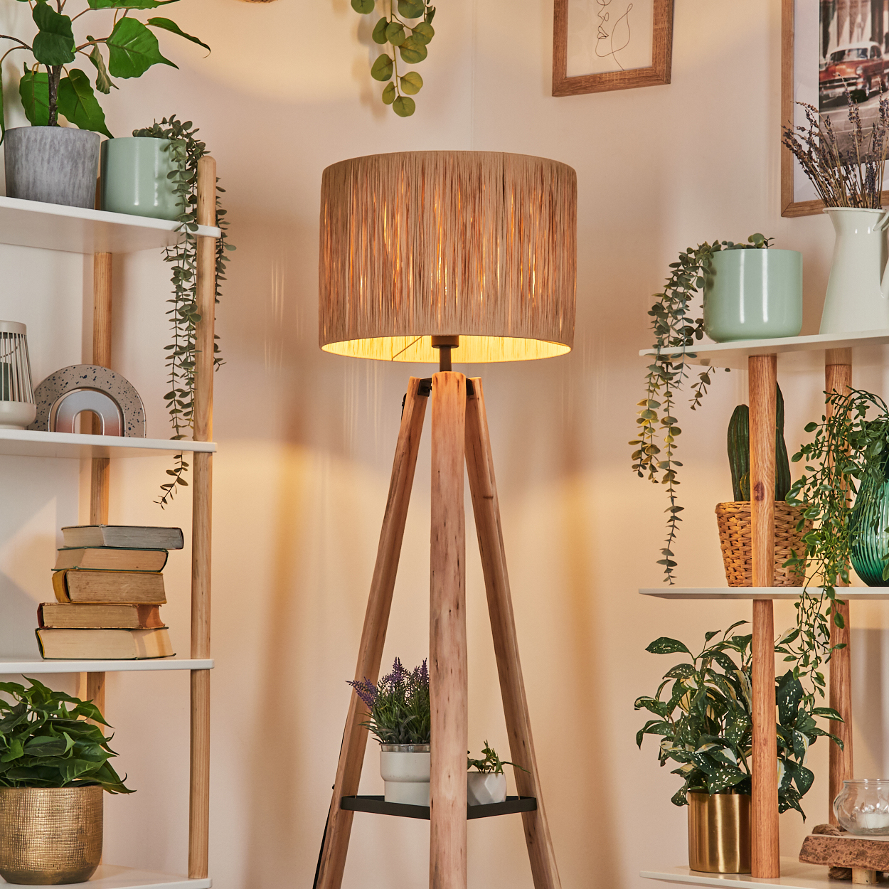 Eine Stehlampe aus Holz steht in einem gemütlichen Raum. Regale mit Pflanzen und Büchern umgeben sie. Die Lampe hat einen strukturierten Lampenschirm.