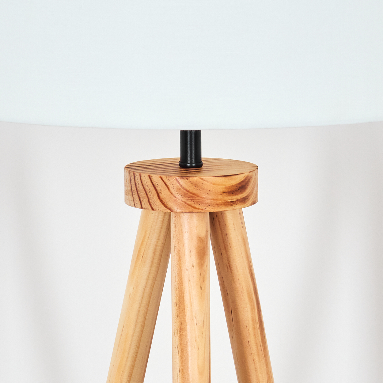 Eine Stehlampe mit Holzstativ und weißem Lampenschirm. Die Holzbeine sind hellbraun, der obere Teil ist dunkler.
