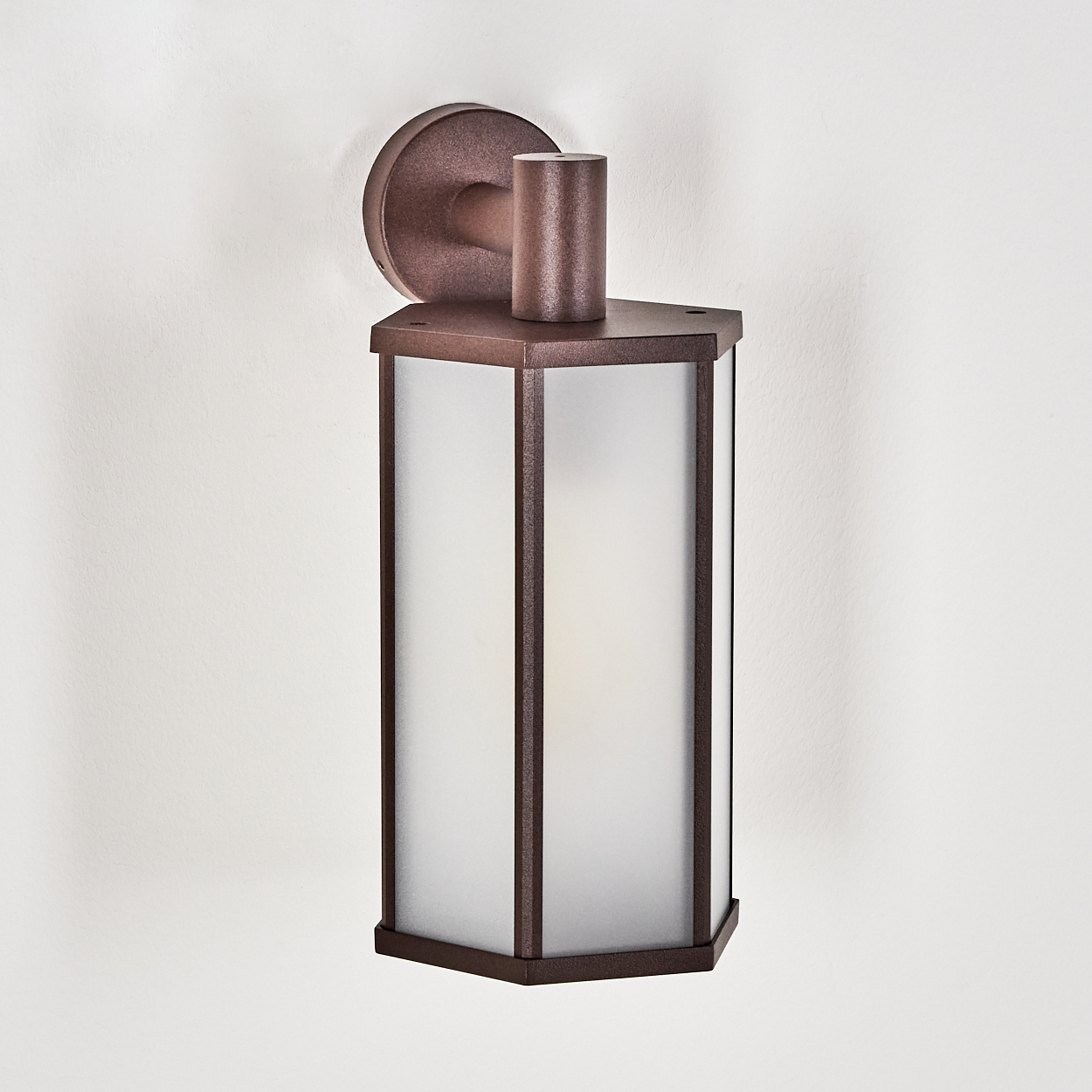 Eine bronzefarbene Außenwandleuchte mit mattiertem Glasschirm. An einer weißen, strukturierten Wand montiert. Die Leuchte hat eine zylindrische Oberseite.