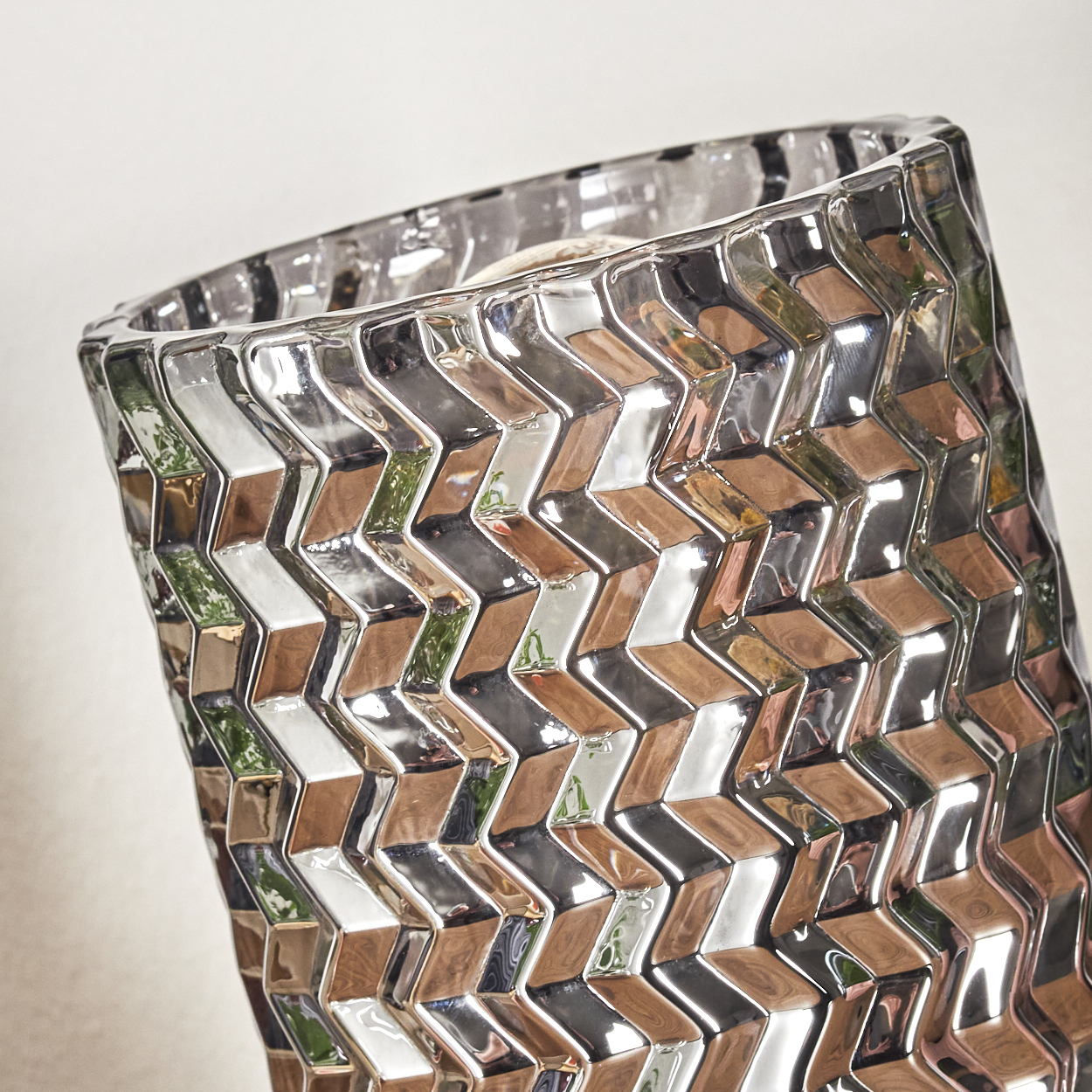 Dekorative, strukturierte Glasvase mit Zickzackmuster. Die Vase reflektiert die Farben der Umgebung, heller Hintergrund.