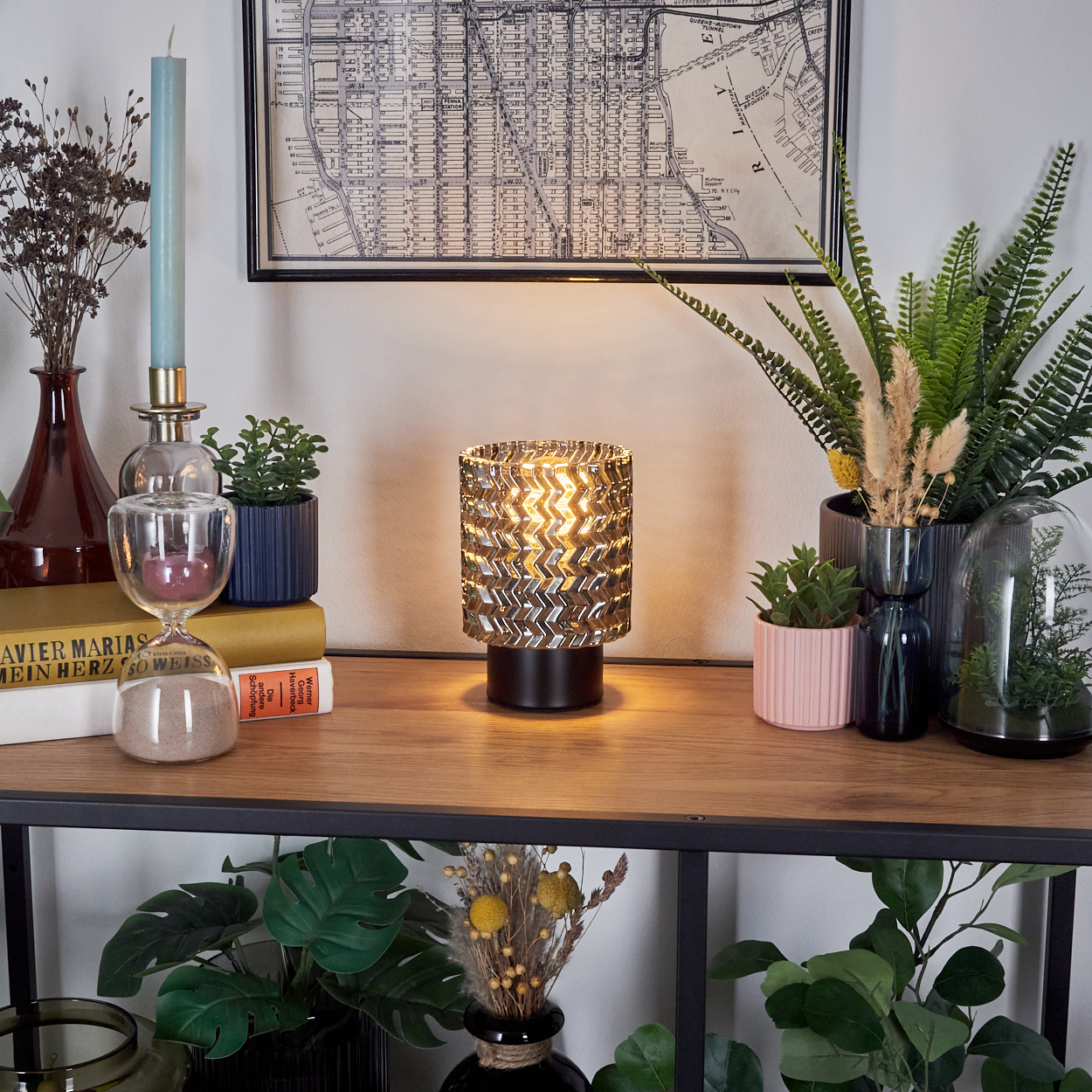 Eine beleuchtete Lampe auf einem Holzregal mit Pflanzen, Büchern, einer Karte und dekorativen Gegenständen. Pflanzen befinden sich davor und dahinter.