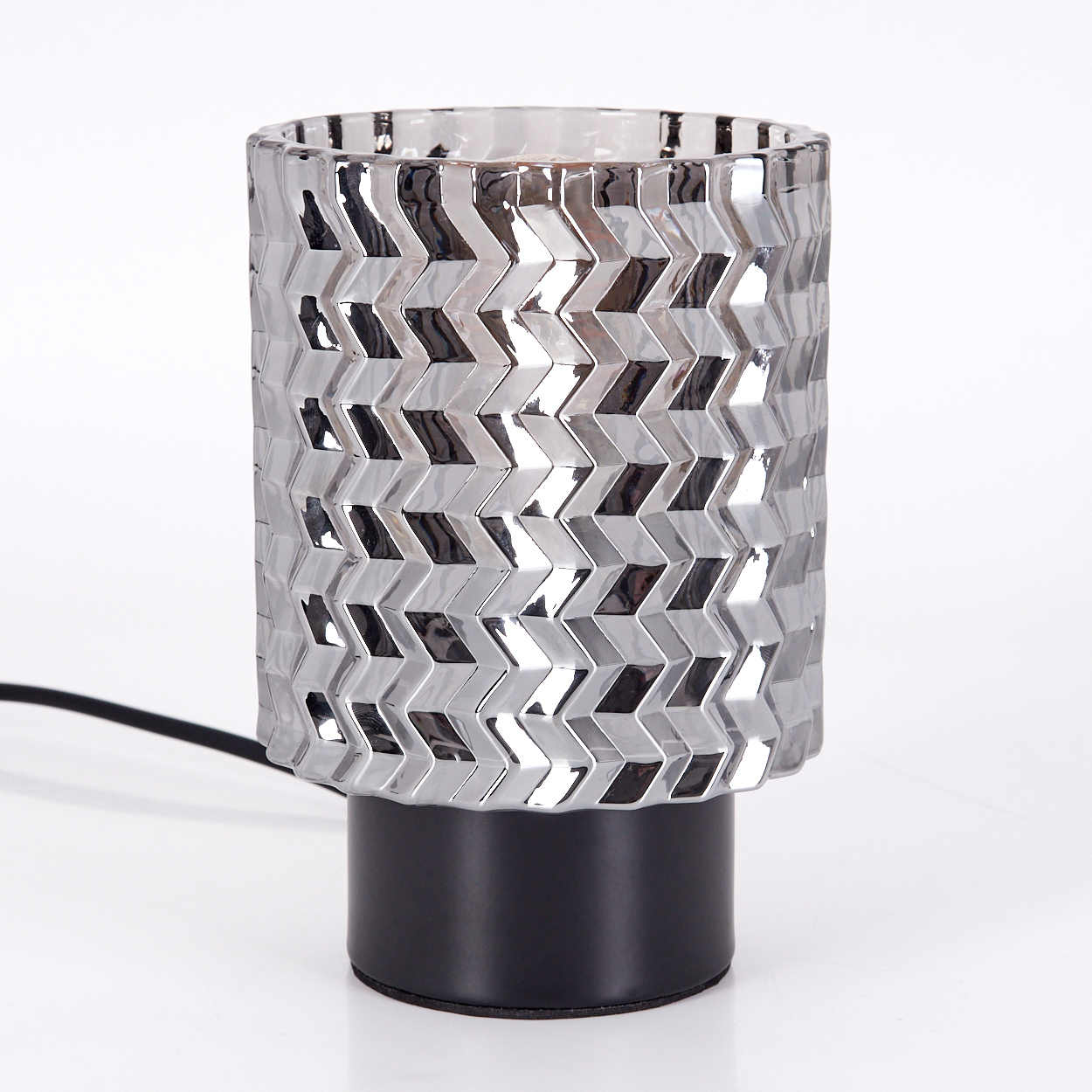 Silberne Lampe mit Zickzackmuster auf schwarzem Sockel. Ein schwarzes Kabel geht von der Lampe aus. Der Hintergrund ist weiß.