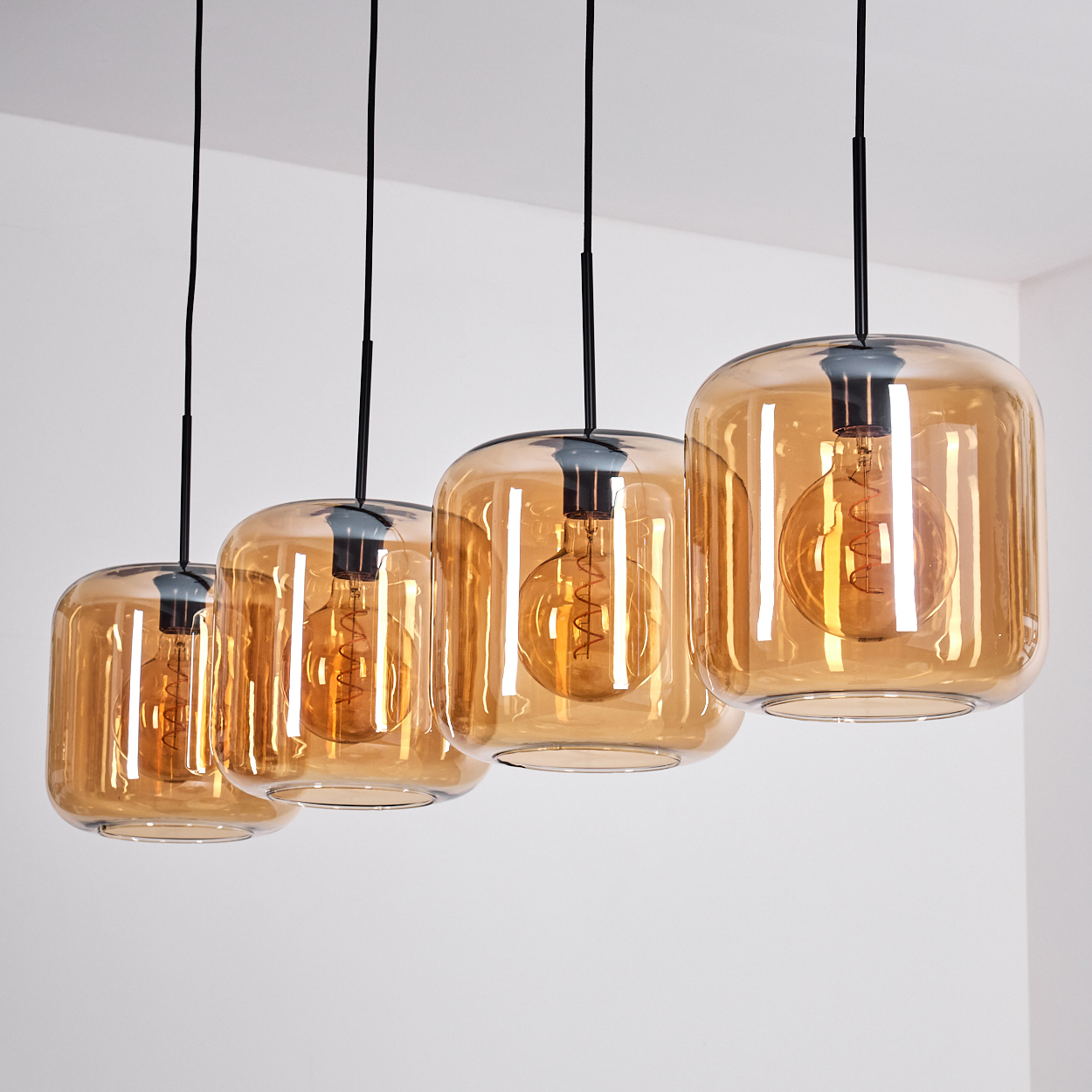 Vier bernsteinfarbene Pendelleuchten hängen von der Decke. Jede hat einen Glasschirm mit einer sichtbaren Glühbirne.