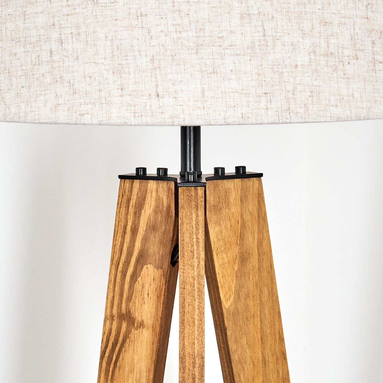 Eine hölzerne Stativ-Stehlampe mit beigefarbenem Lampenschirm. Die Beine der Lampe sind aus Holz. Der Lampenschirm ist beige.