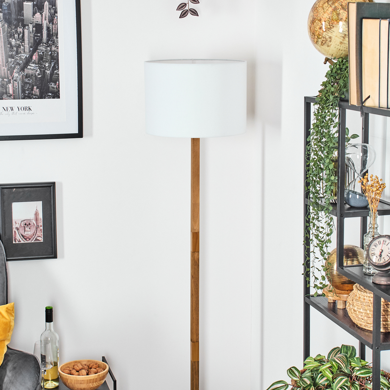Ein Raum mit einer Lampe, Kunst und einem Bücherregal. Die Lampe ist aus Holz und hat einen weißen Schirm. Es gibt ein schwarz gerahmtes Bild und einen Globus.