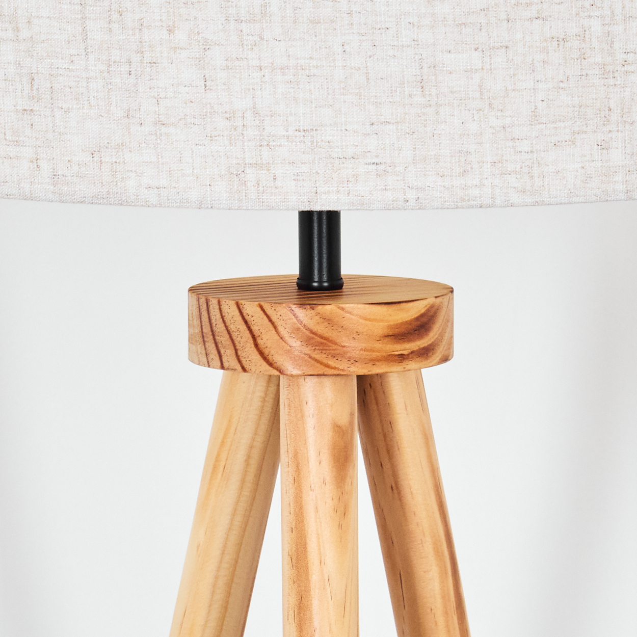 Eine hölzerne Stativlampe. Sie hat einen beigefarbenen Lampenschirm und einen Holzsockel. Der Hintergrund ist weiß.
