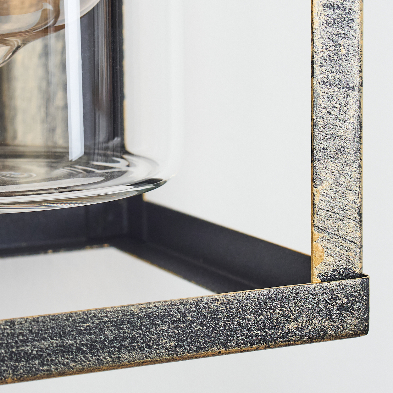 Nahaufnahme eines Glasbehälters in einem Metallrahmen. Der Rahmen ist schwarz und gold, mit strukturierter Oberfläche. Hintergrund ist weiß.