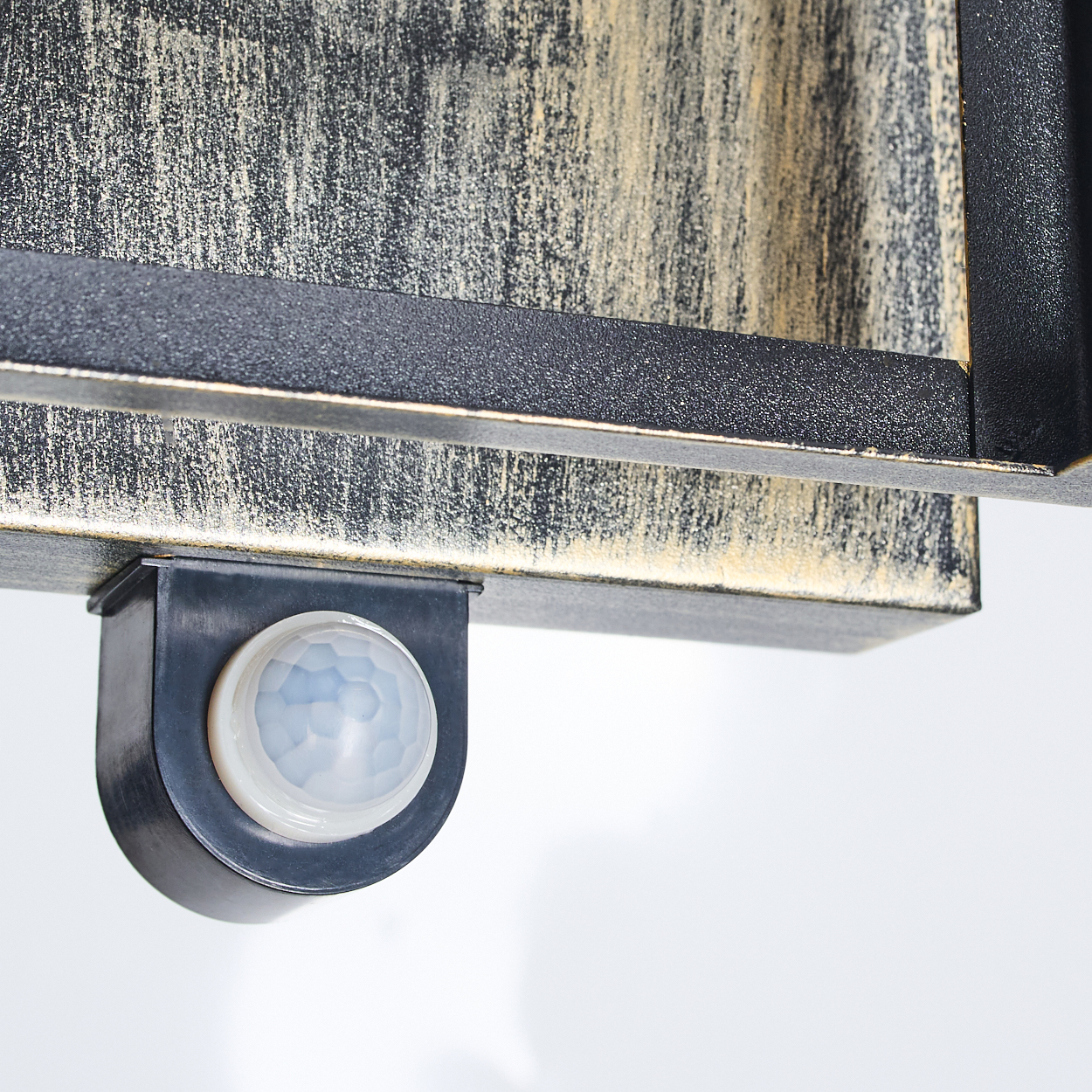 Nahaufnahme einer schwarz-goldenen Halterung mit Bewegungssensor. Der Sensor ist weiß und blau, vor weißem Hintergrund.