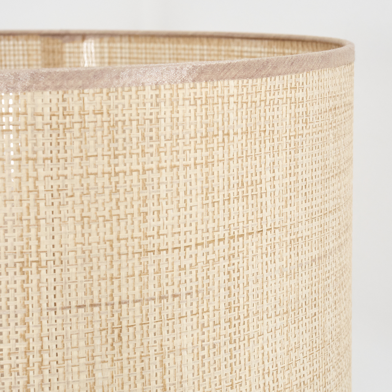 Nahaufnahme eines Lampenschirms. Er ist aus hellbeige Material gewebt. Der obere Rand ist dunkler beige. Weißer Hintergrund.