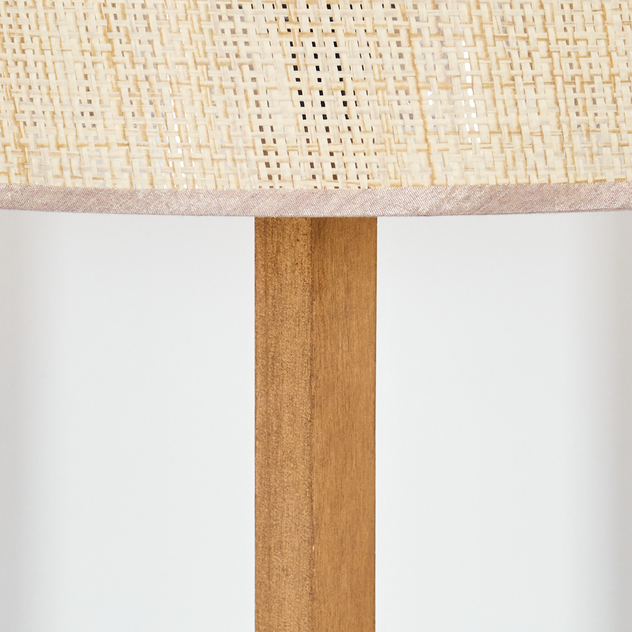 Eine Lampe mit gewebtem Lampenschirm und Holzfuß. Der Hintergrund ist schlicht weiß.