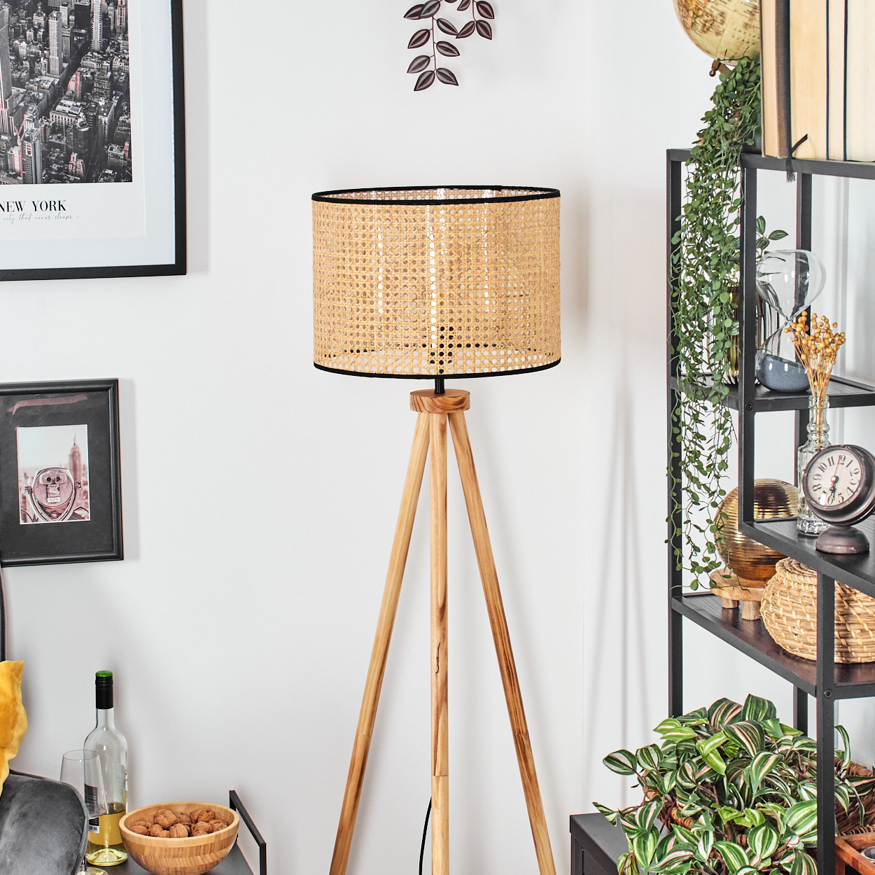 Eine Holz-Stativlampe mit gewebtem Schirm steht in einem Raum mit Bücherregal, Bildern und Pflanzen.