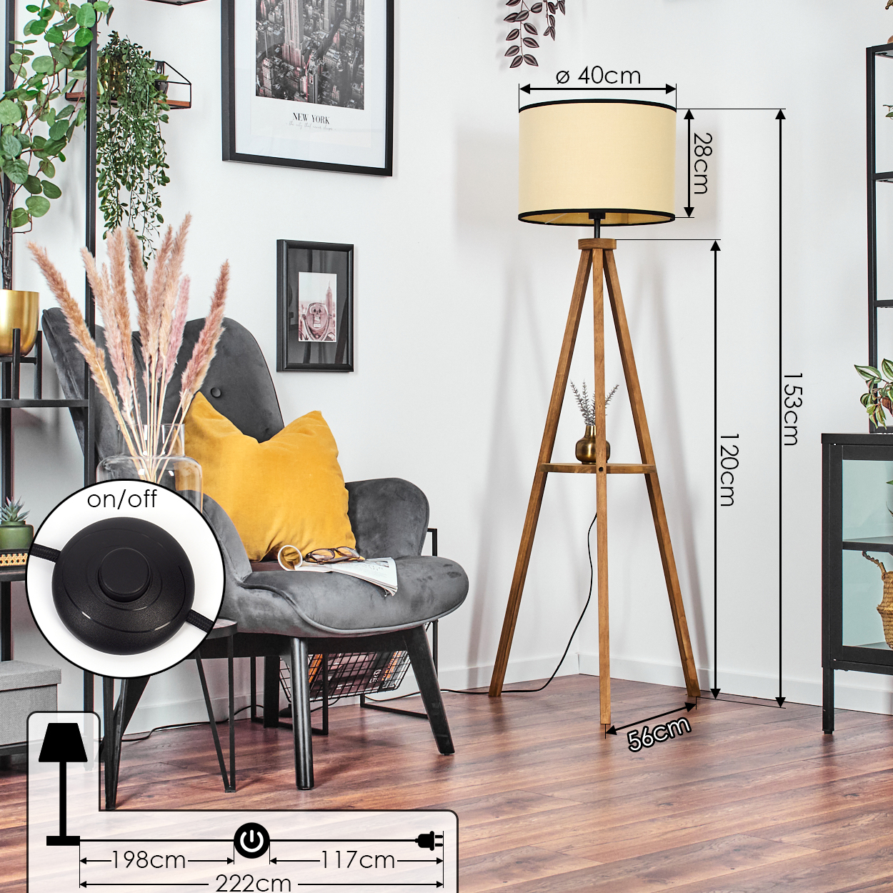 Ein Raum mit einer hölzernen Stativ-Stehlampe, einem Sessel mit gelbem Kissen und einem schwarz gerahmten Bild an der Wand.