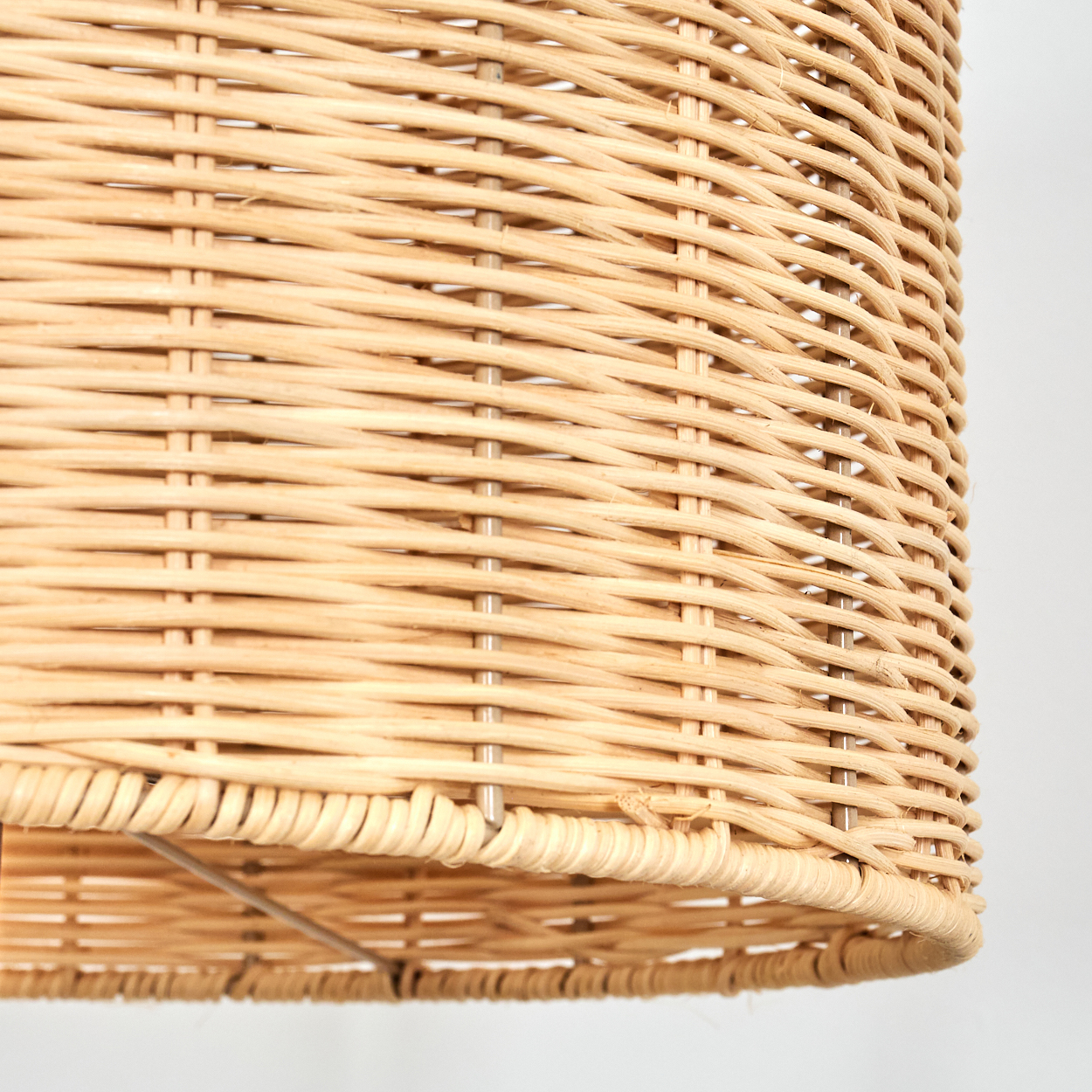 Nahaufnahme eines geflochtenen Lampenschirms aus Rattan. Die Farbe ist hellbraun und das Webmuster ist sichtbar. Der Hintergrund ist weiß.