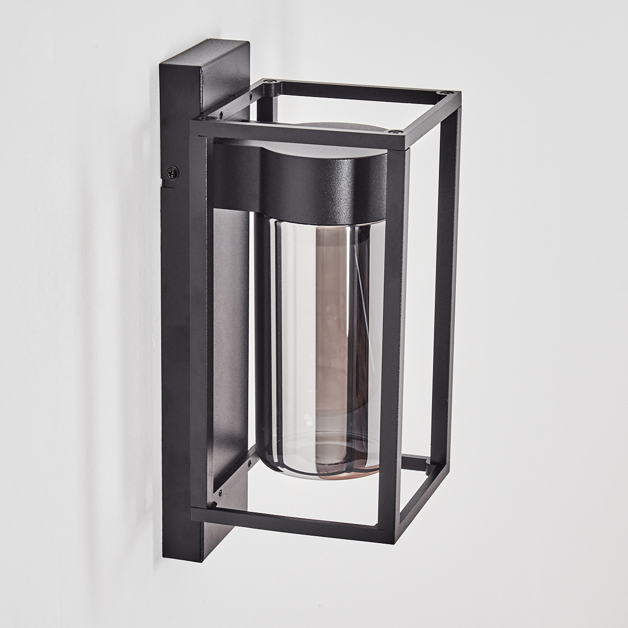 Eine schwarze Außenlampe aus Metall ist an einer weißen Wand montiert. Sie hat einen rechteckigen Rahmen und einen Glaszylinder.