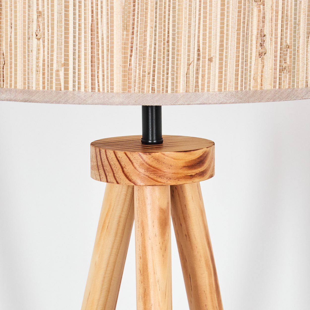 Nahaufnahme einer Holzstativlampe. Beiger Lampenschirm, Holzsockel und drei Holzbeine. Weißer Hintergrund.