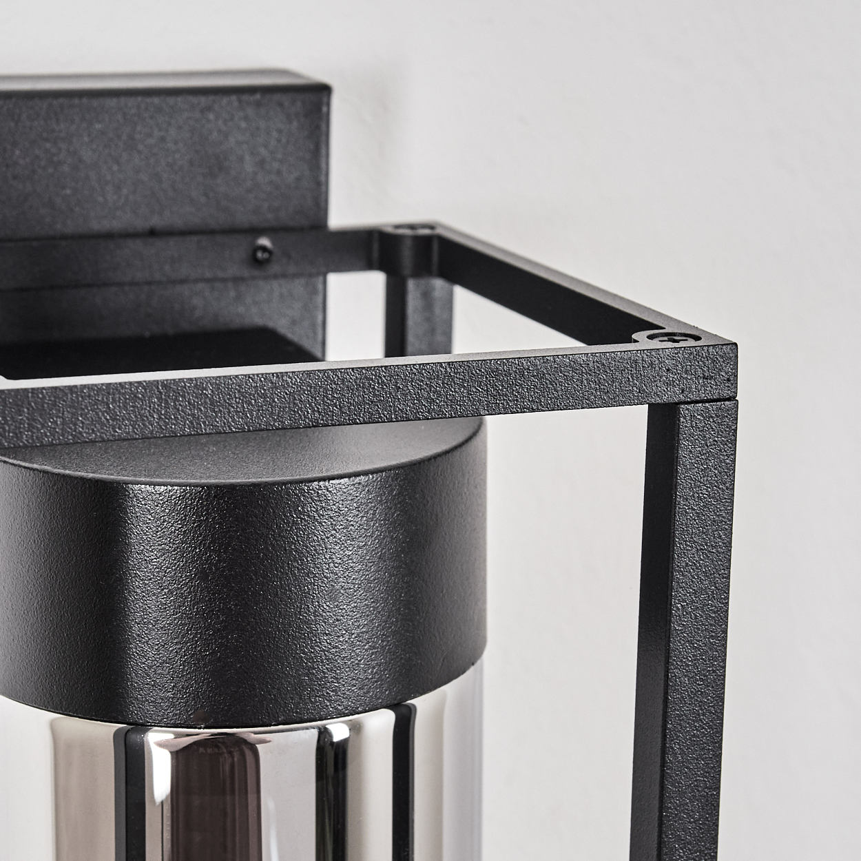 Nahaufnahme einer schwarzen Metalllampe mit quadratischem Rahmen. Die Lampe hat eine zylindrische Basis mit glänzendem, metallischem Finish.