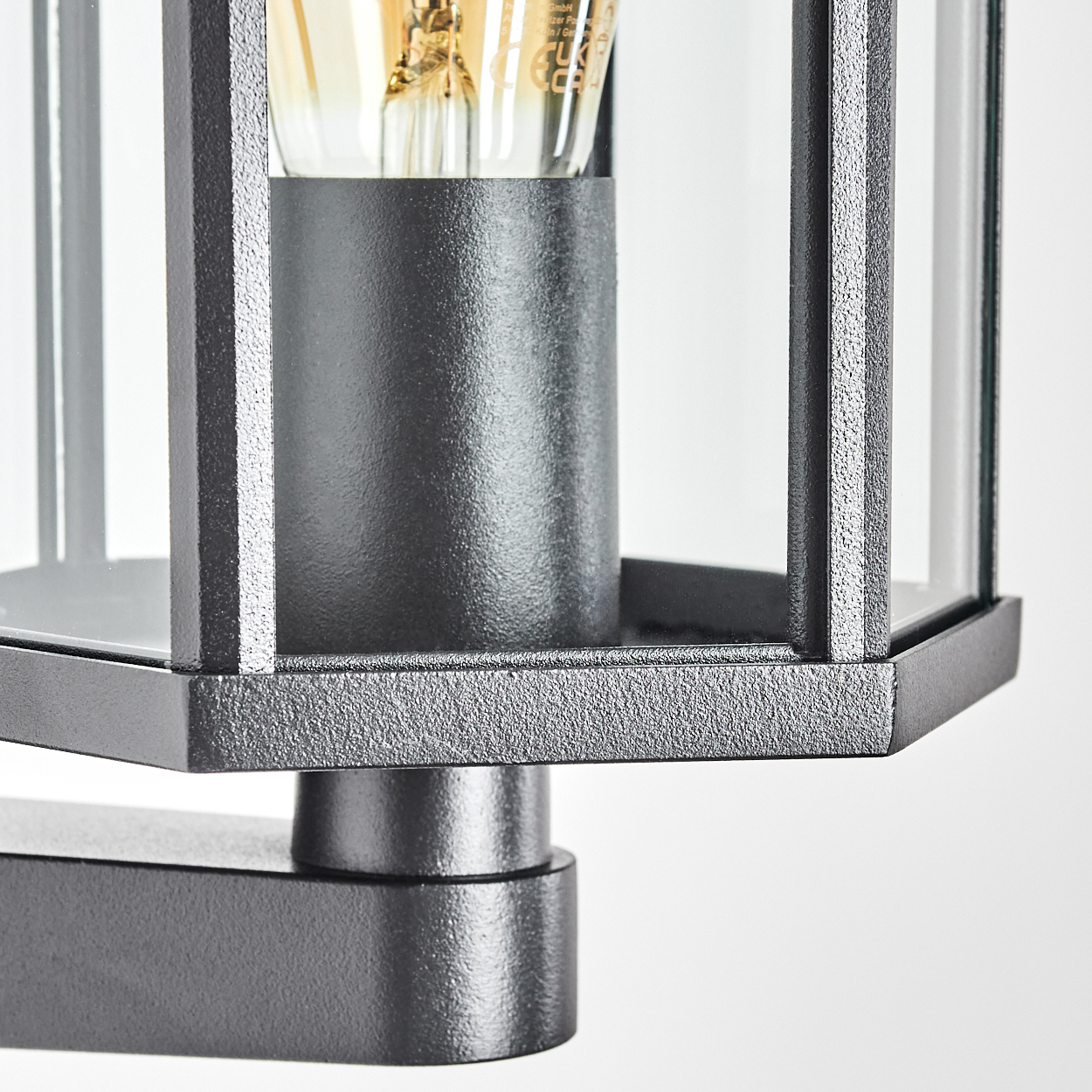 Nahaufnahme einer modernen schwarzen Außenlampe mit Glasscheiben. Im Inneren der Lampe ist eine Glühbirne zu sehen.