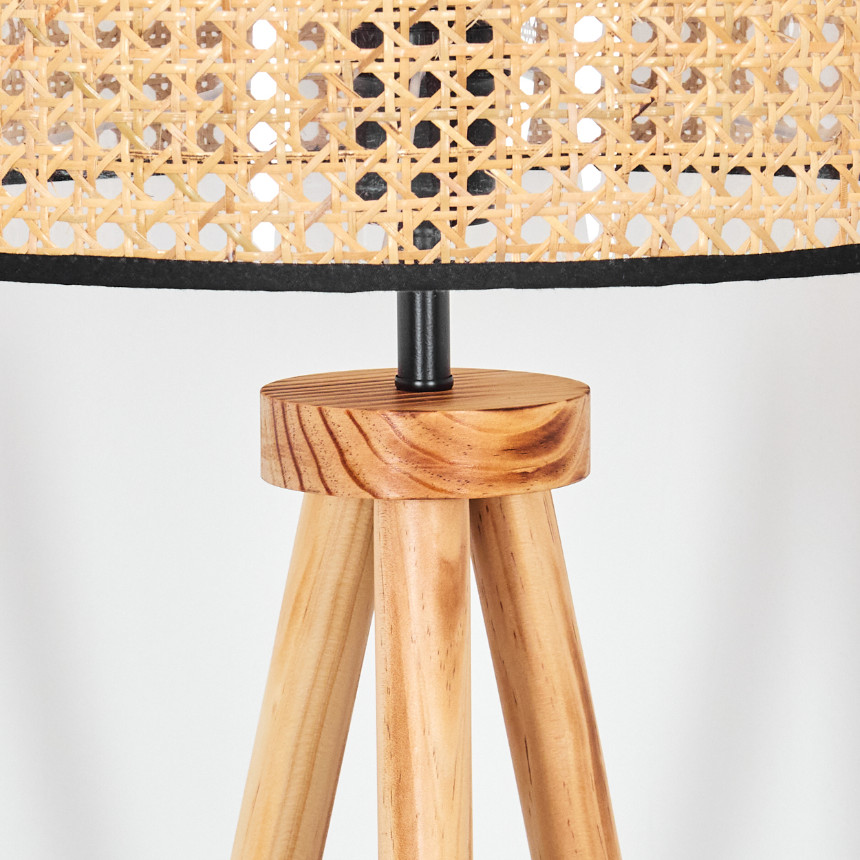 Nahaufnahme einer Holzlampe. Der Schirm ist gewebt, der Fuß ist aus Holz mit drei Beinen, und eine schwarze Metallstange verbindet sie.