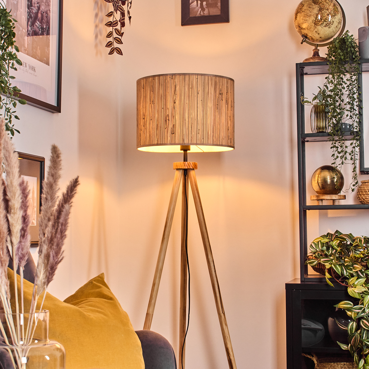 Eine hölzerne Stativlampe, ein gelbes Kissen und ein Regal mit Pflanzen und einem Globus.