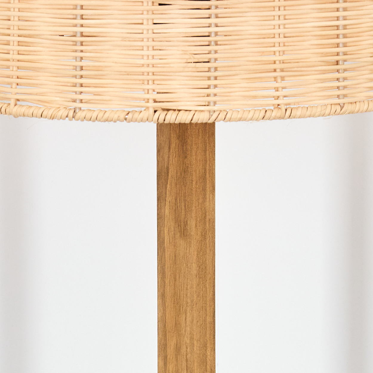 Nahaufnahme einer Lampe. Die Oberseite ist aus geflochtenem, hellbraunem Material, das von einem vertikalen Holzpfosten getragen wird. Der Hintergrund ist weiß.
