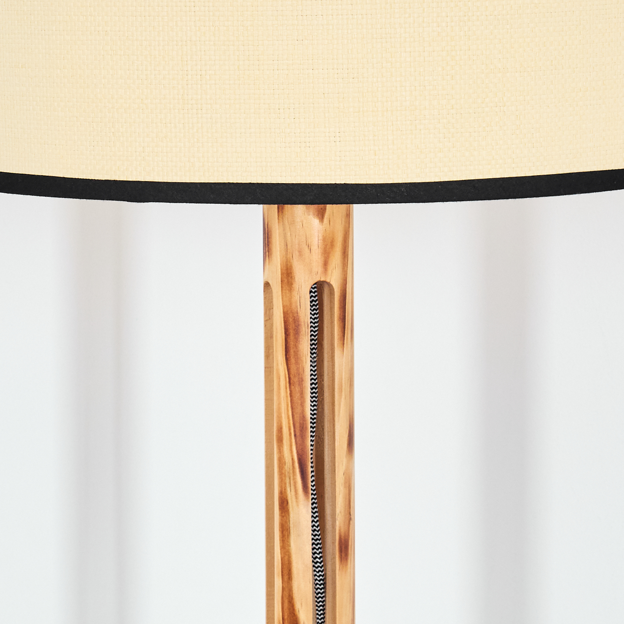 Nahaufnahme einer Holzlampe. Beigefarbener Lampenschirm mit schwarzem Rand, Holzständer mit schwarz-weißem Kabel, weißer Hintergrund.