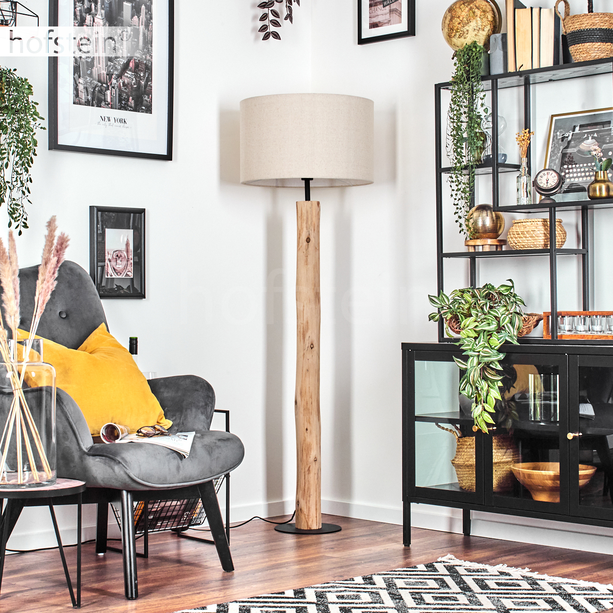Wohnzimmer mit Holz-Stehlampe, Sessel mit gelbem Kissen und schwarzem Regal mit Dekoration.