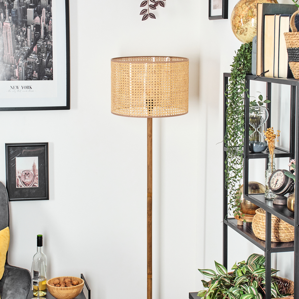 Ein Raum mit einer Rattanlampe, einem Regal mit Büchern und einem Bild von New York. Es gibt einen Tisch mit einer Weinflasche und Nüssen.